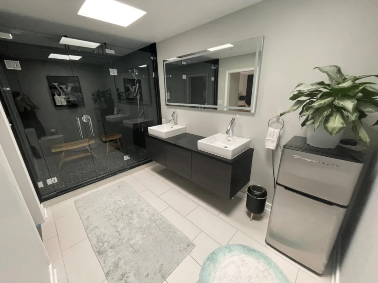 Modern bathroom with double vanity, large mirror, walk-in glass shower, and plant
