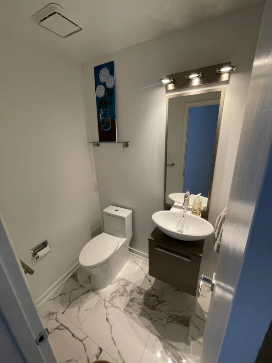 Small bathroom with a toilet, vessel sink in a dark vanity, wall mirror, and marble-patterned floor