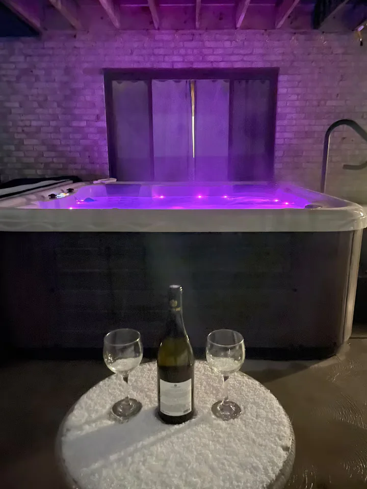 Illuminated purple hot tub beside a wine bottle and two wine glasses