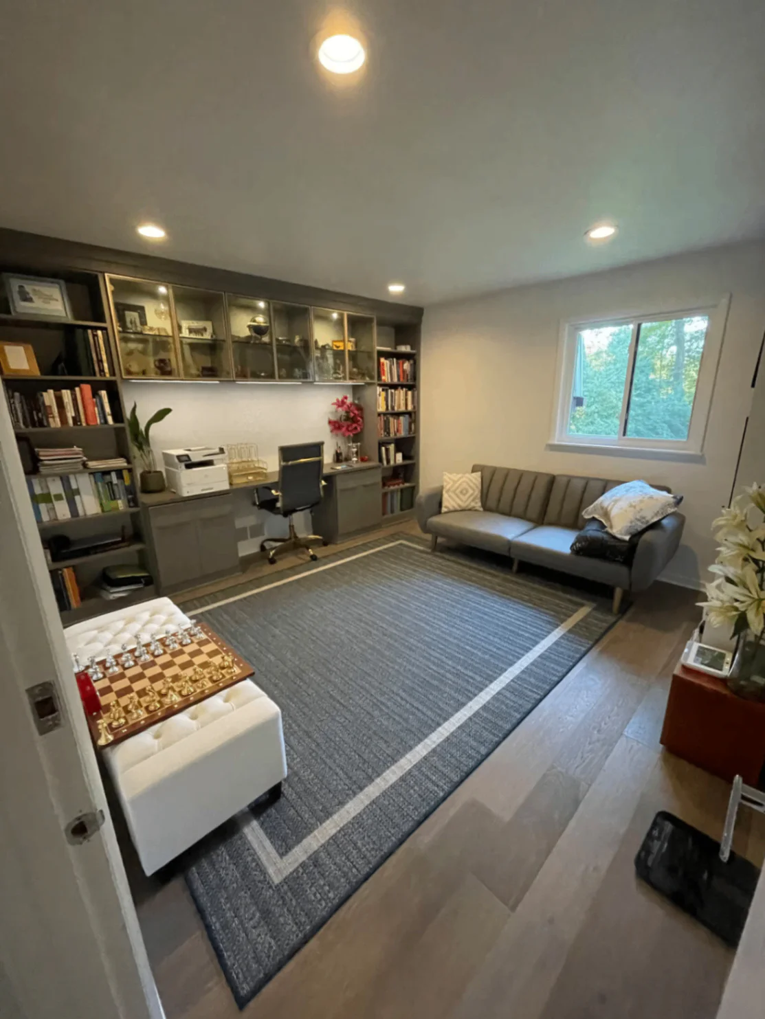 Home office with bookshelves, desk, printer, sofa, chess set, and window view