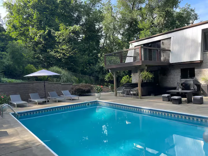 Outdoor swimming pool with patio loungers, umbrella, terrace, and house