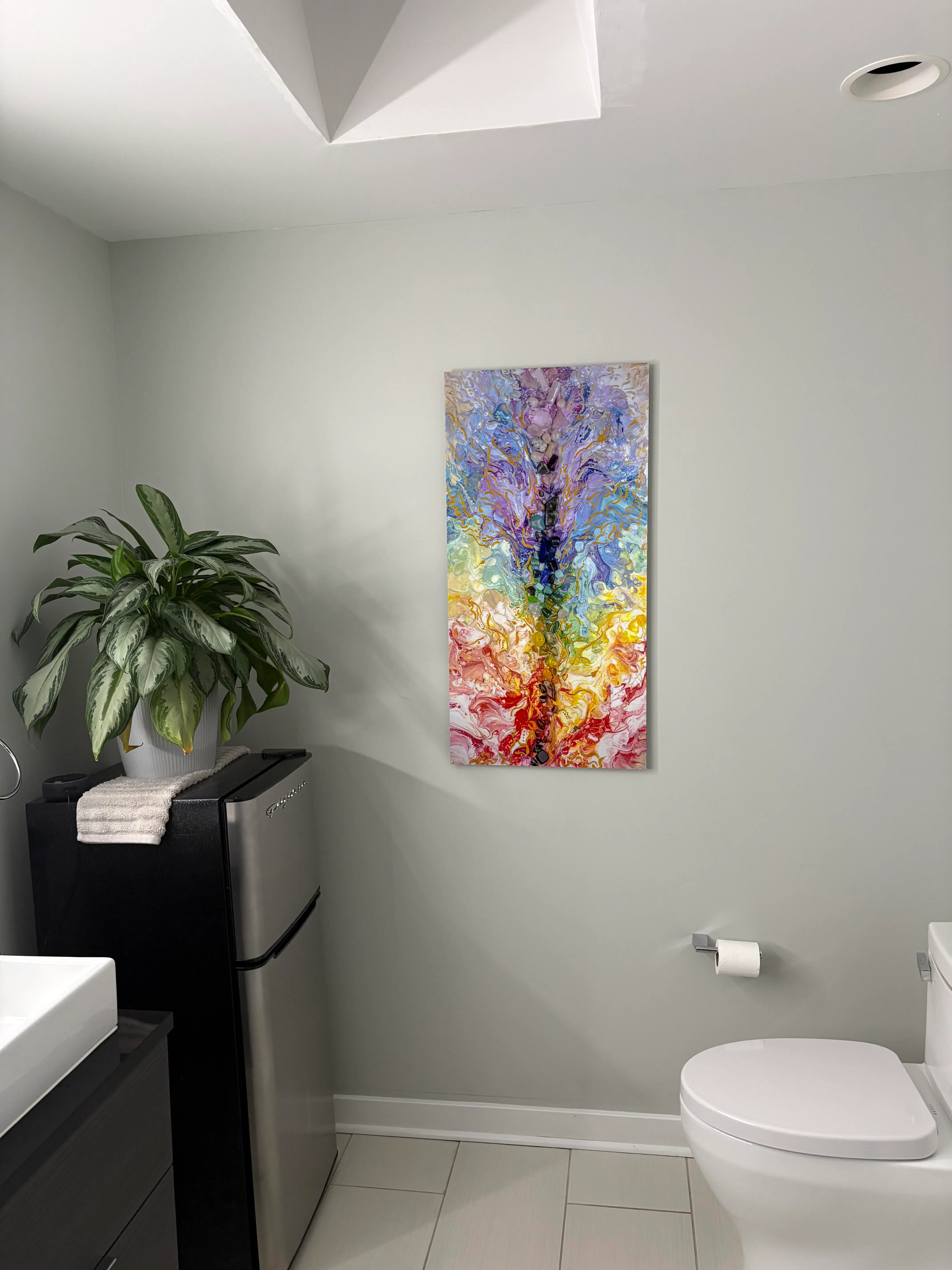 Colorful abstract painting hung on a bathroom wall beside a plant