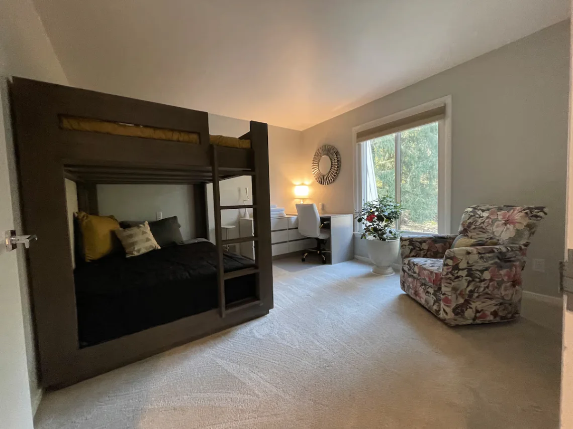The Dormitory bedroom with bunk bed, desk, forest-facing window, and floral chair.