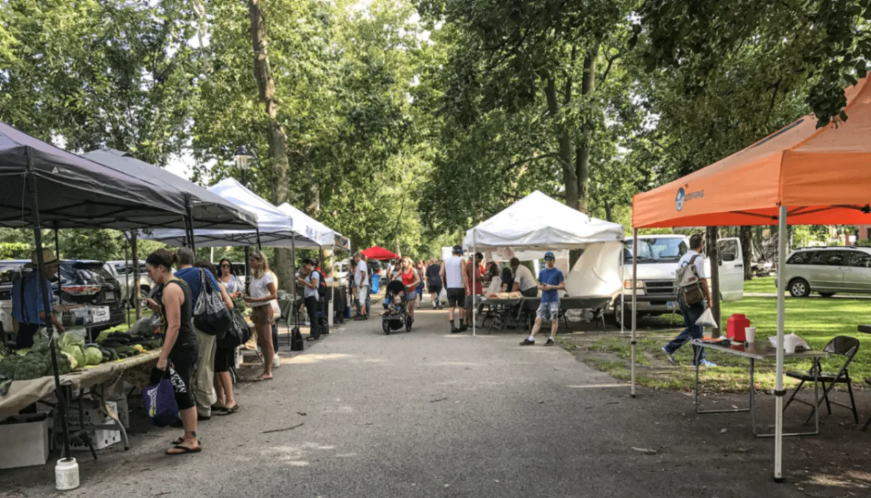 Farmers market vendors and shoppers in a tree-lined Pittsburgh park