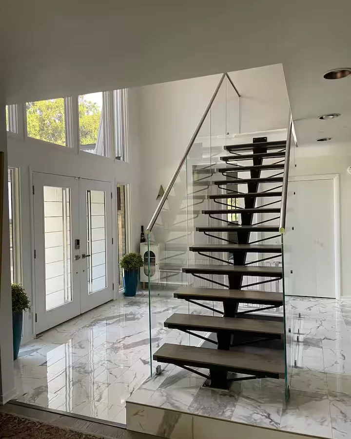 Bright Posh entry foyer with white double doors, marble floor, glass railing, and floating staircase.